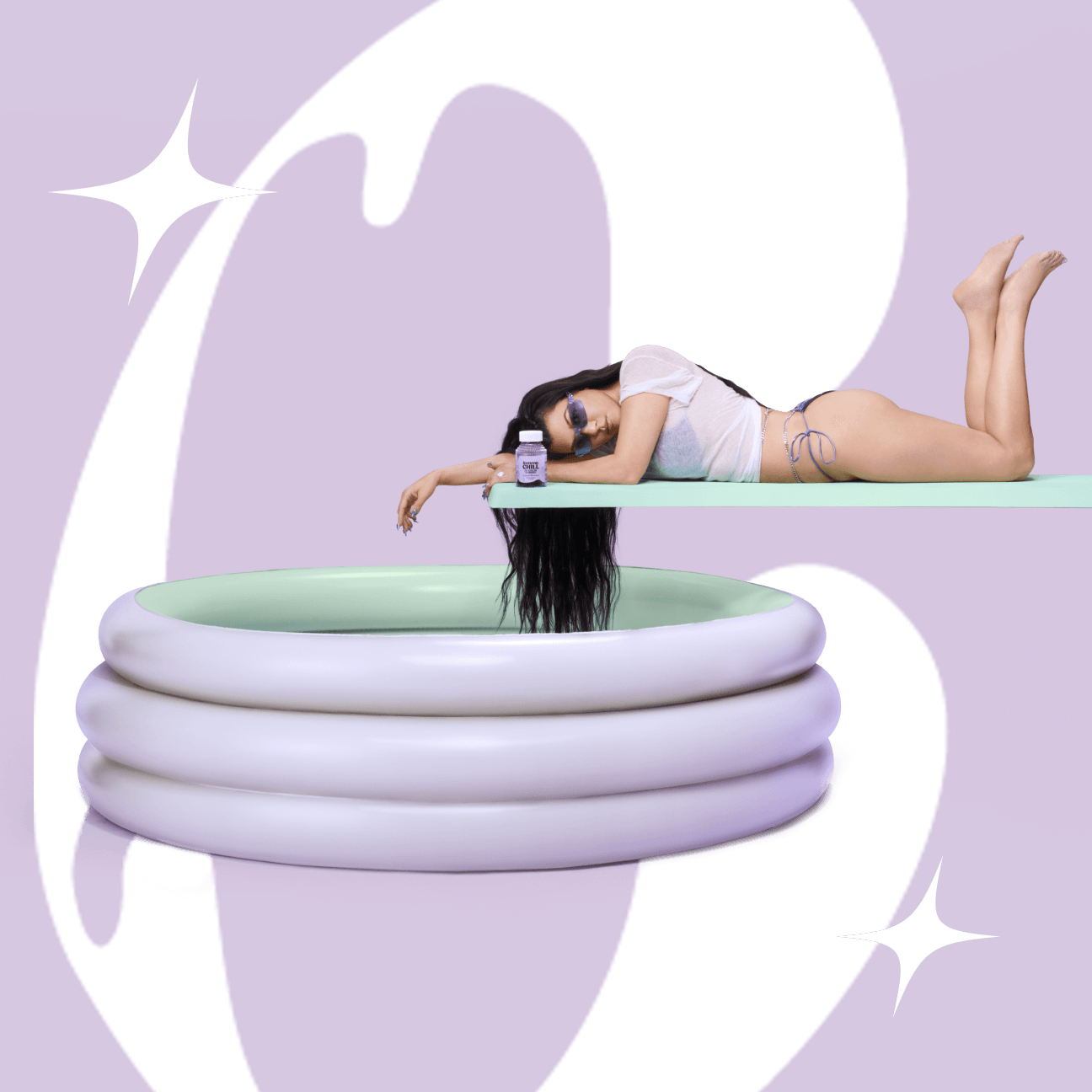 Kourtney laying on a diving board with a bottle of Lemme Chill beside her. A wading pool sits beneath the diving board